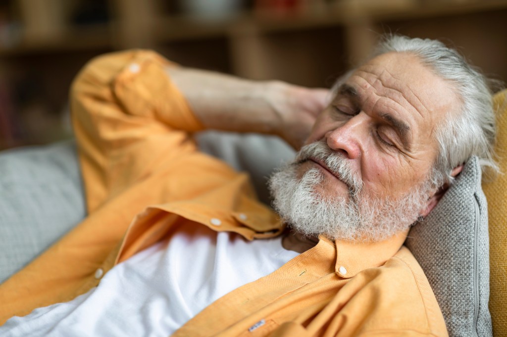Senior man's foreground photo sleeping with long beard, a quiet grandfather who rests on the couch home, enjoying the noon nap in the living room. Concept of the lifestyle of the elderly